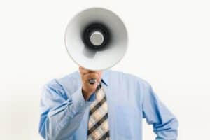 A person in a blue shirt and striped tie holds a megaphone, like criminal defense lawyers Louisiana making their voice heard.