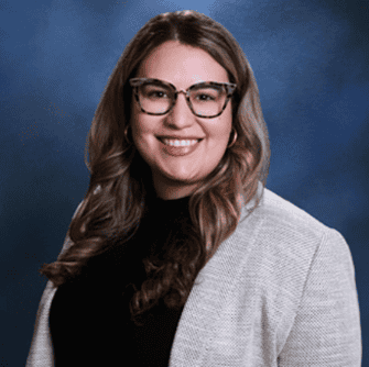 Woman with long wavy hair, glasses, and a light blazer over a black top, smiling like one of the top personal injury lawyers Louisiana trusts.