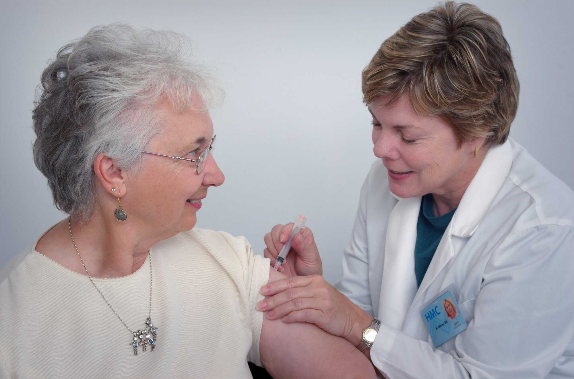 A healthcare professional gives an older woman a vaccination shot in her upper arm in a clinical setting, like louisiana immigration lawyers help clients.
