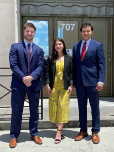 Three people stand outside glass doors labeled 707; two men in suits flank a woman in a yellow floral outfit—criminal defense lawyers Louisiana.