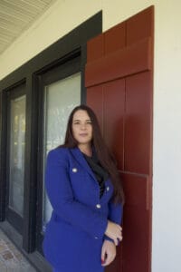 A woman with long brown hair in a blue blazer stands before a building, evoking the confidence of immigration lawyers Louisiana clients trust.