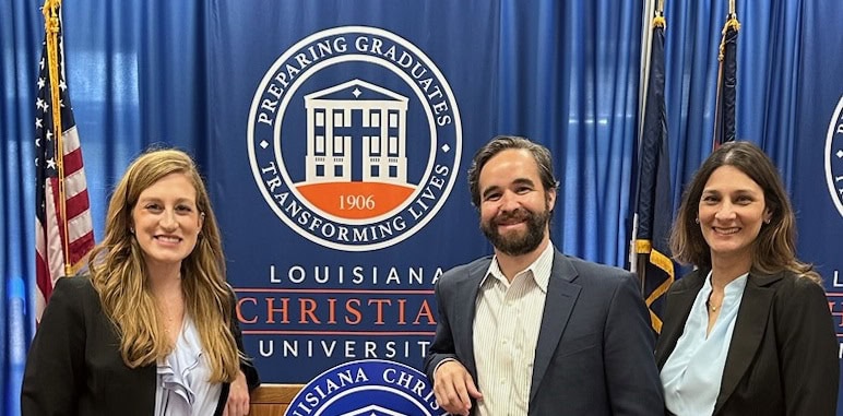Three people in business attire stand smiling before a Louisiana Christian University banner, joined by personal injury lawyers Louisiana.