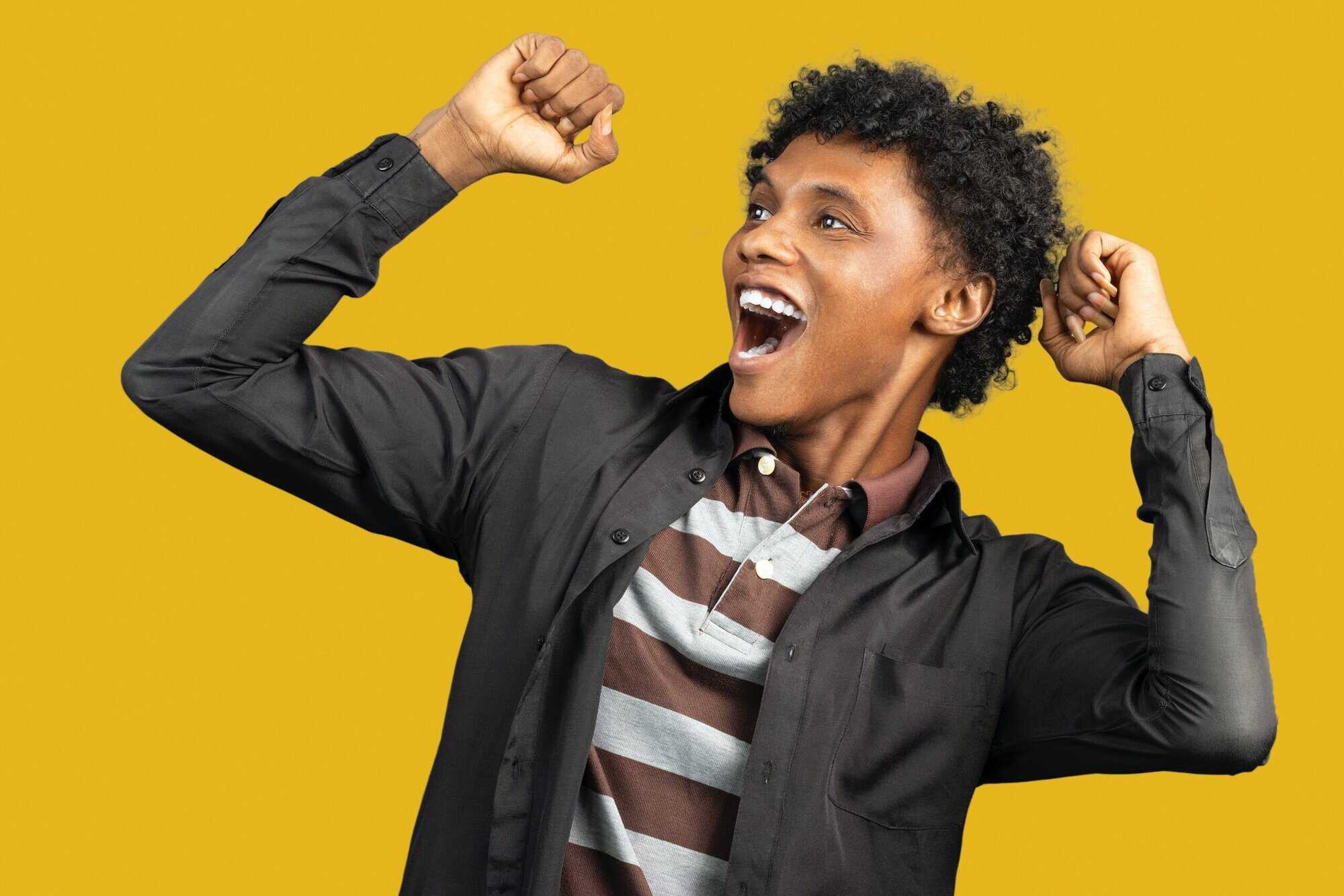 A person in a striped shirt and black jacket raises both arms, smiling widely like victorious criminal defense lawyers Louisiana, against yellow.