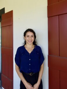 A person with dark hair in a blue shirt—possibly one of Louisiana's top personal injury lawyers—stands smiling in front of red shutters.