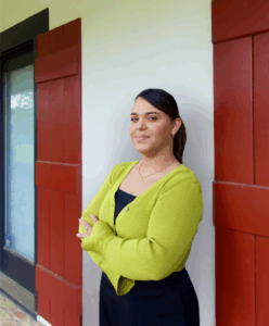 A woman with long dark hair, wearing a green cardigan, stands with her arms crossed outside a personal injury lawyers Louisiana office.
