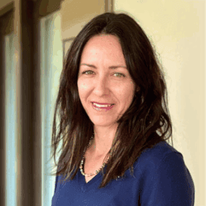 A woman with long dark hair, possibly a personal injury lawyer in Louisiana, smiles indoors wearing a navy top and beaded necklace.