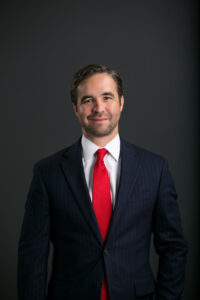 Man in a dark pinstripe suit, white shirt, and red tie stands confidently—ideal for visa lawyers or immigration lawyers Louisiana profiles.