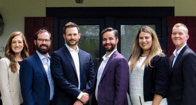 Six people in business attire, including criminal defense lawyers Louisiana, pose outdoors for a group photo in front of a building entrance.