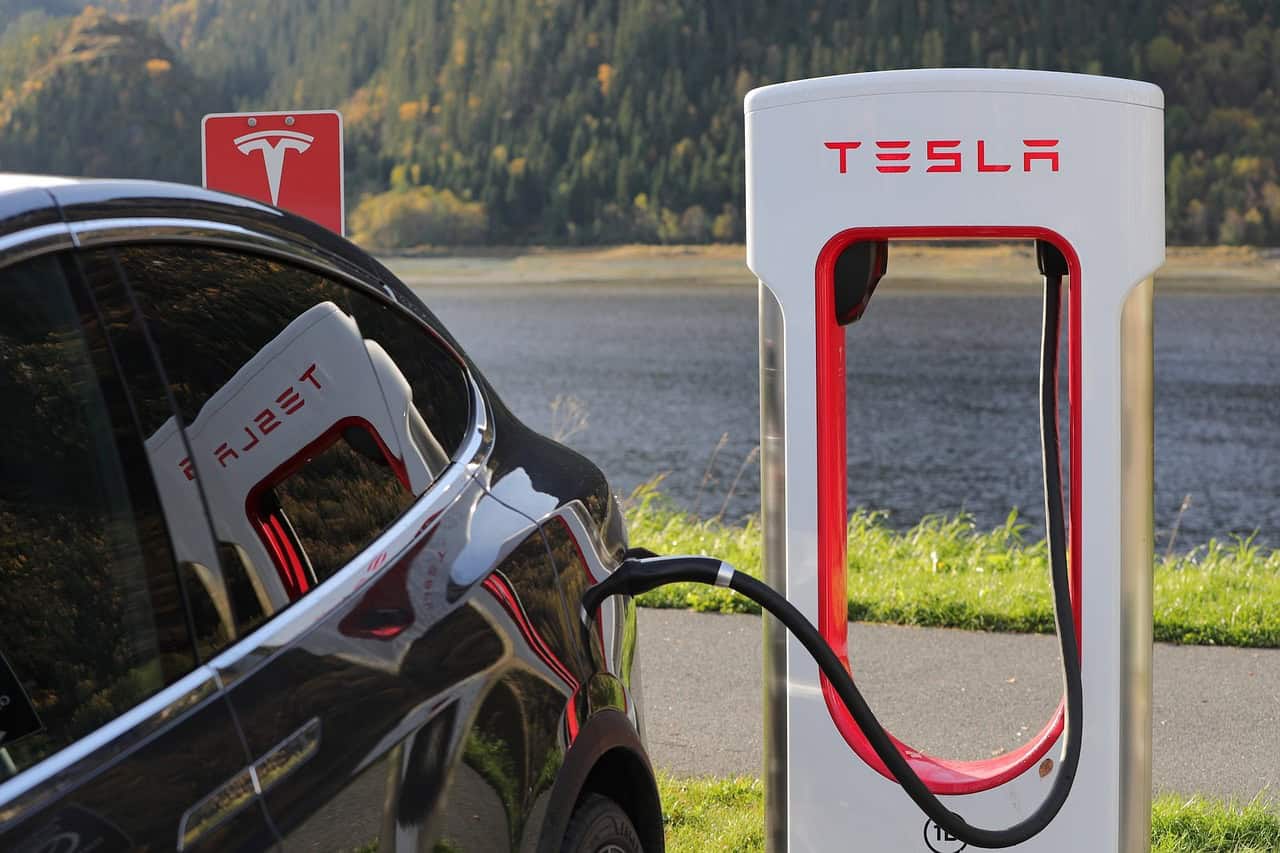 A Tesla electric car charges at a Supercharger station near water and trees, similar to how Louisiana immigration lawyers power your legal journey.