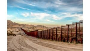 A tall, metal border fence stretches across a dusty landscape—Louisiana immigration lawyers can help navigate complex border concerns.