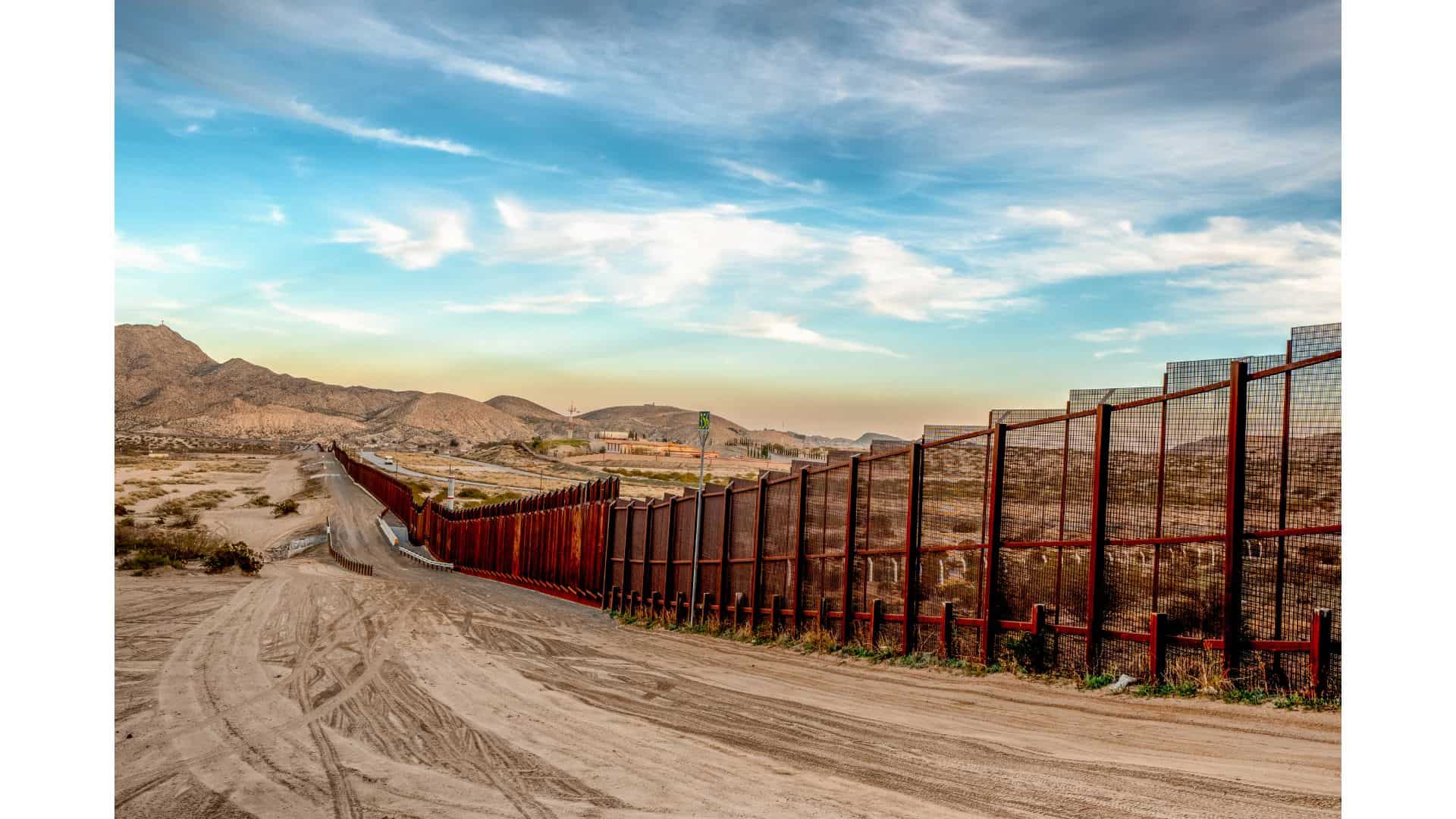 A tall, metal border fence stretches across a dusty landscape—Louisiana immigration lawyers can help navigate complex border concerns.