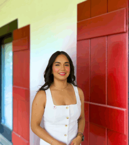 A woman with dark hair in a white dress stands smiling in front of a wall with large red shutters, like those at personal injury lawyers Louisiana.
