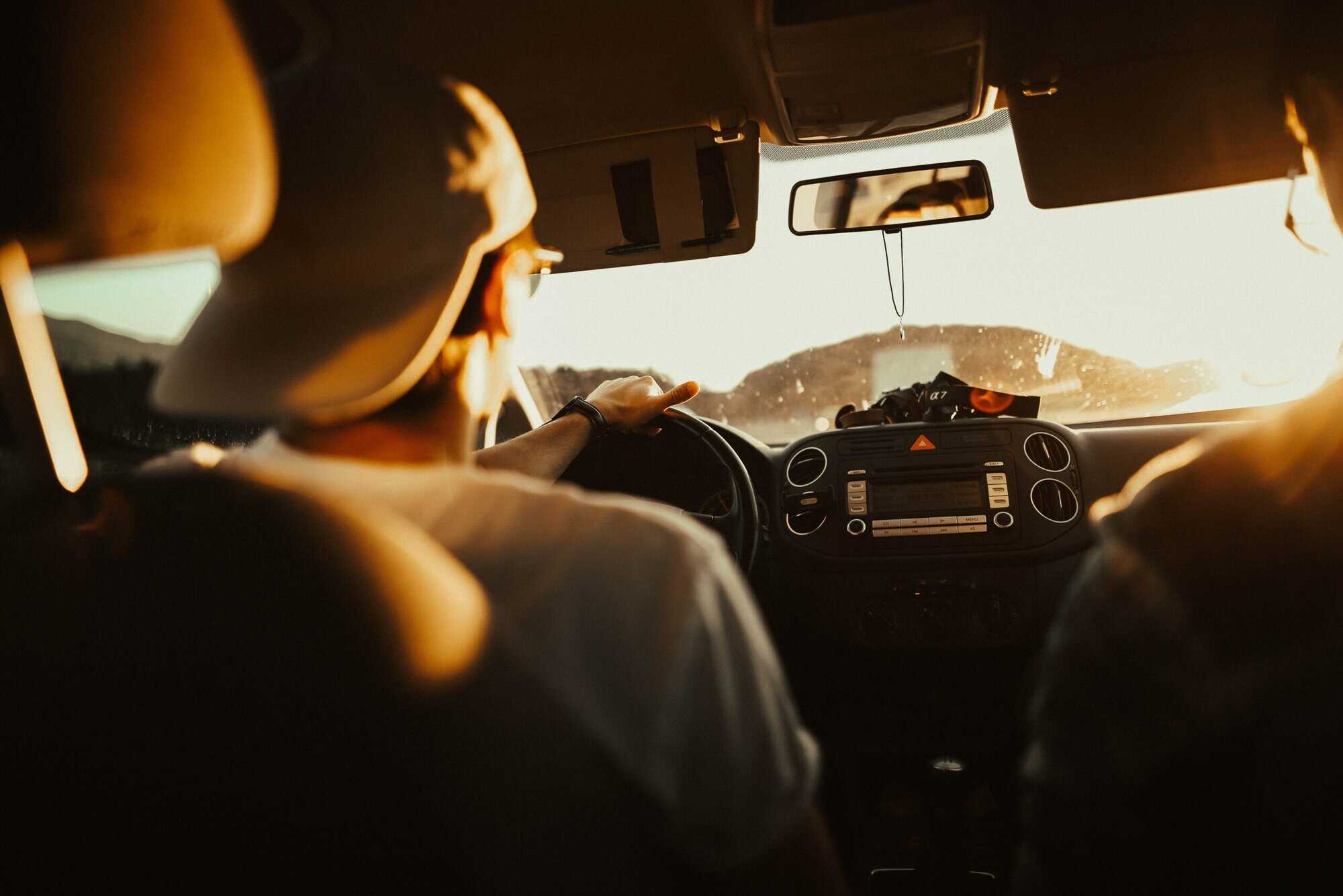 Person wearing a cap drives at sunset, sunlight streaming in, while discussing with a passenger about Louisiana immigration lawyers.