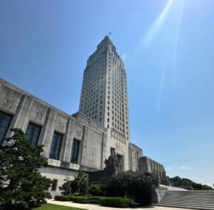 Tall art deco state capitol stands amid greenery, sunlight glinting—home to trusted criminal defense lawyers Louisiana relies on.