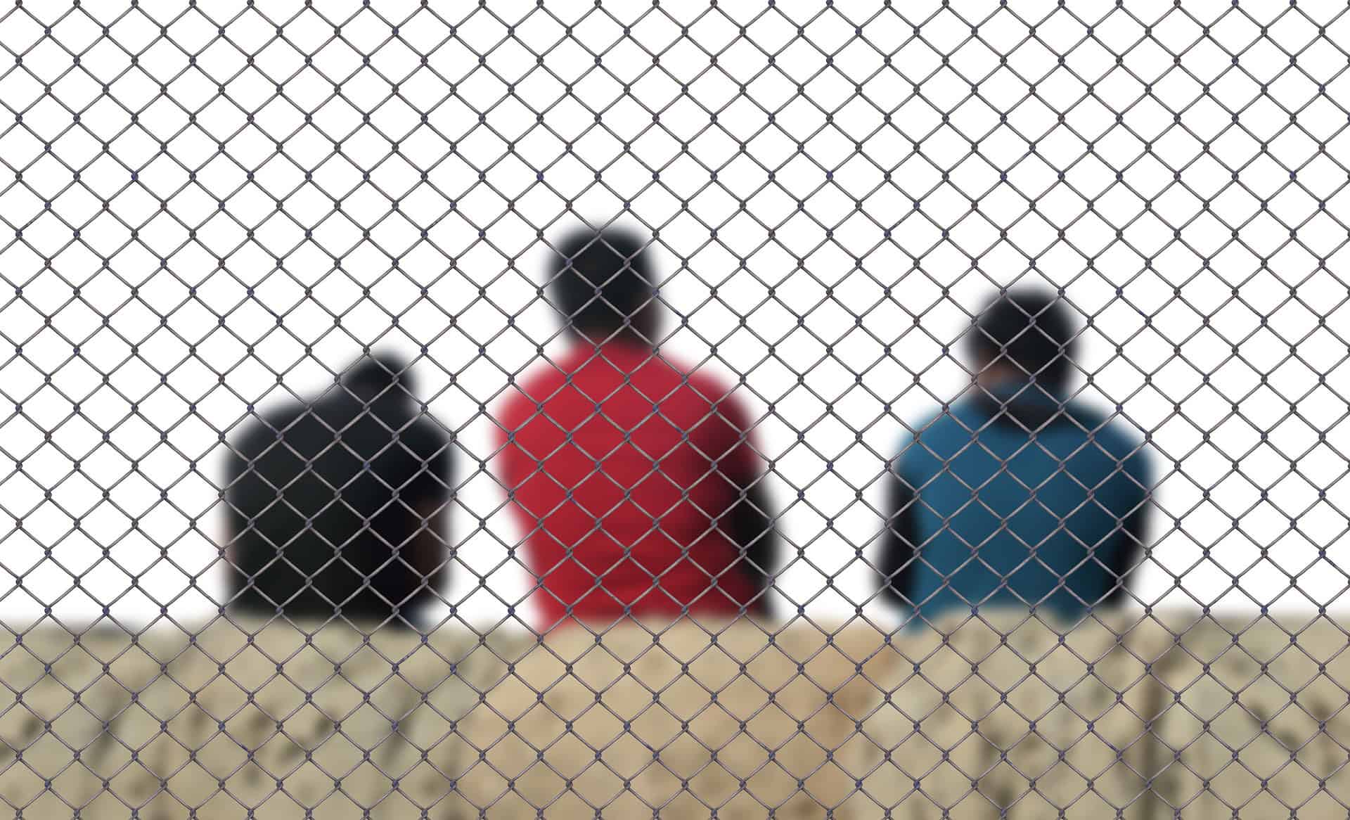 Three people sit on a ledge behind a chain-link fence, evoking themes Louisiana immigration lawyers address every day.