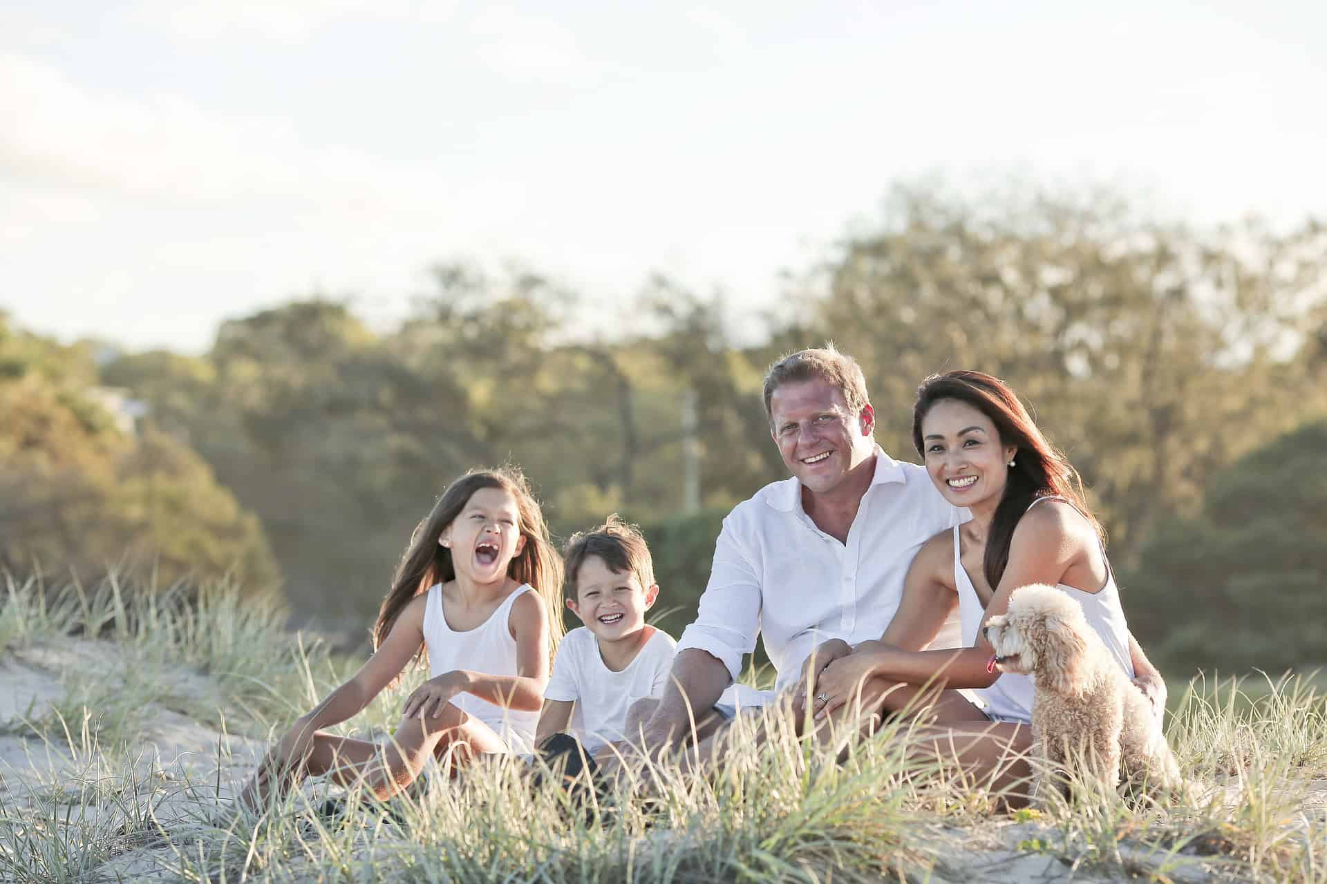 A family of four and their small dog sit on sandy grass, smiling outdoors; Louisiana immigration lawyers can help families like theirs.