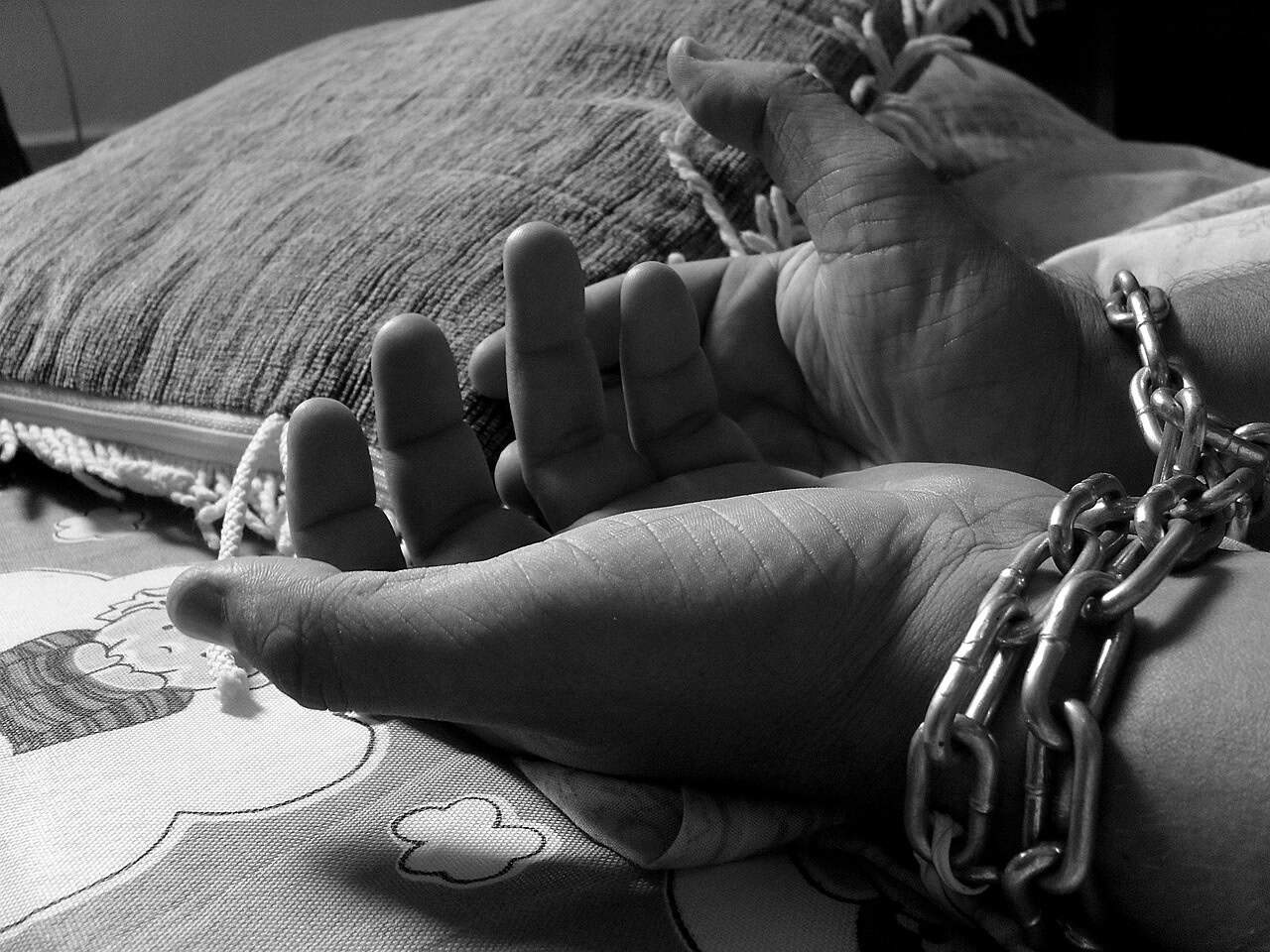 A pair of hands in chains resting on a bed next to a pillow, shown in black and white—criminal defense lawyers Louisiana.