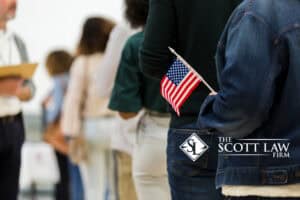People stand in a line, one holding a small American flag. The Scott Law Firm, louisiana immigration lawyers, logo appears in the lower right corner.