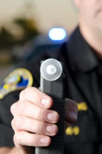 A police officer holds a breathalyzer device, with a police car and blue light behind—a scene often handled by personal injury lawyers Louisiana.