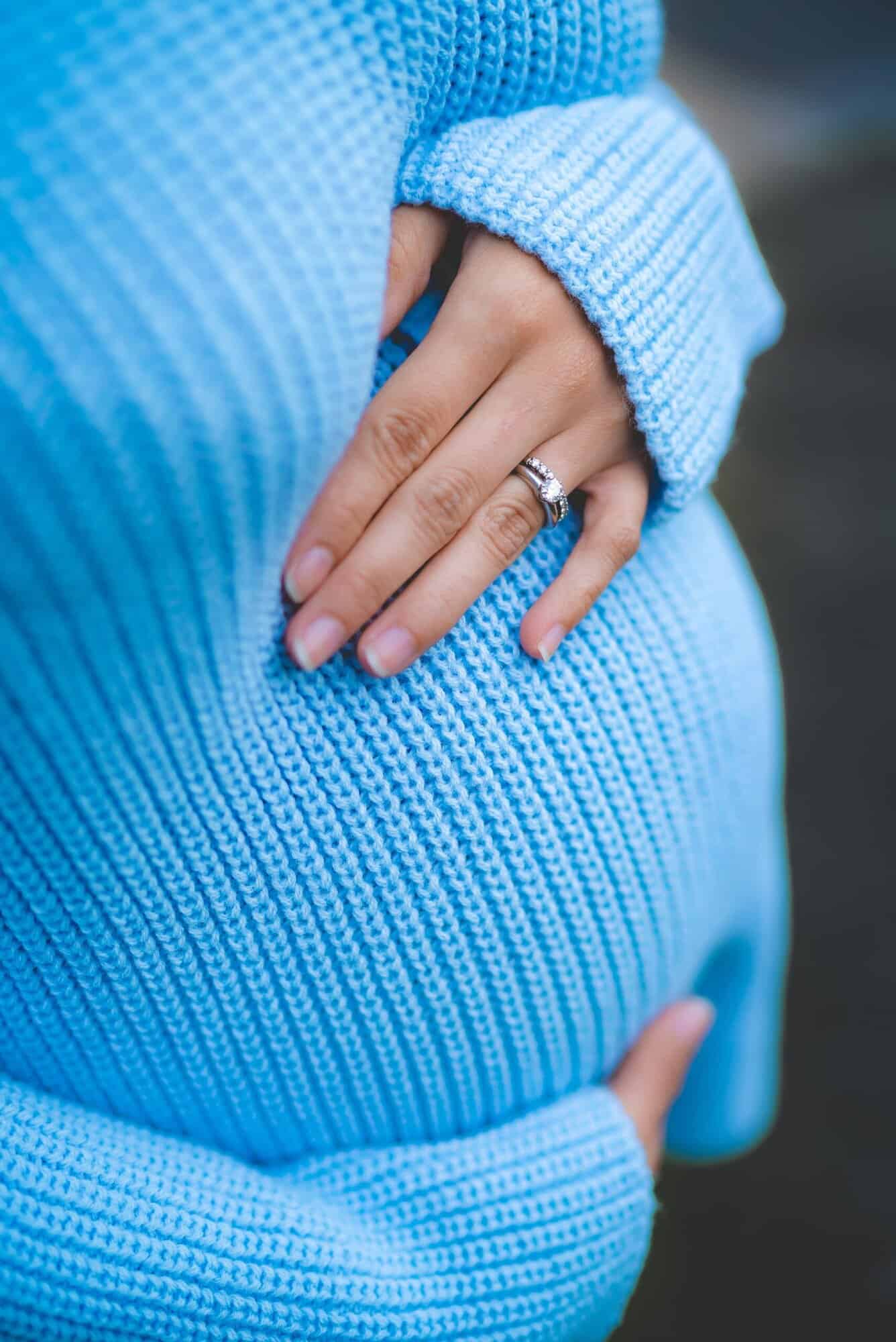 A person in a blue knit sweater is holding their pregnant belly, showing a ring—like criminal defense lawyers Louisiana safeguarding futures.