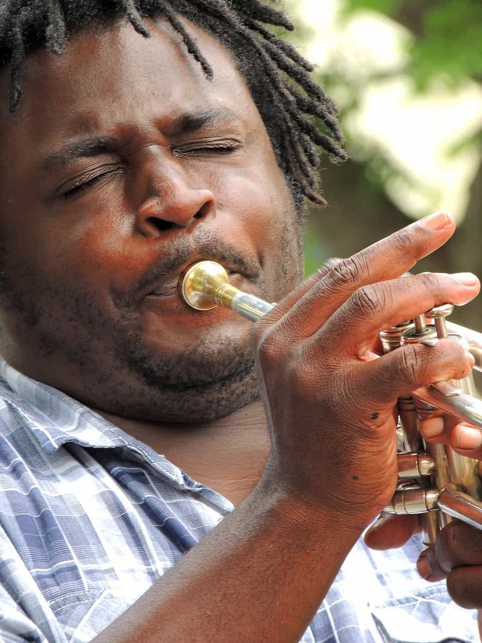 A person in a plaid shirt plays a brass trumpet outdoors, reminiscent of the spirit found at Louisiana immigration lawyers’ gatherings.