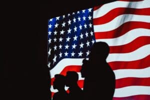 Silhouettes of people stand before a brightly lit American flag, evoking themes central to louisiana immigration lawyers.