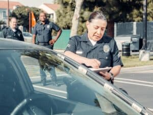 A police officer writes a ticket next to a car as two others look on—much like personal injury lawyers Louisiana review case details.