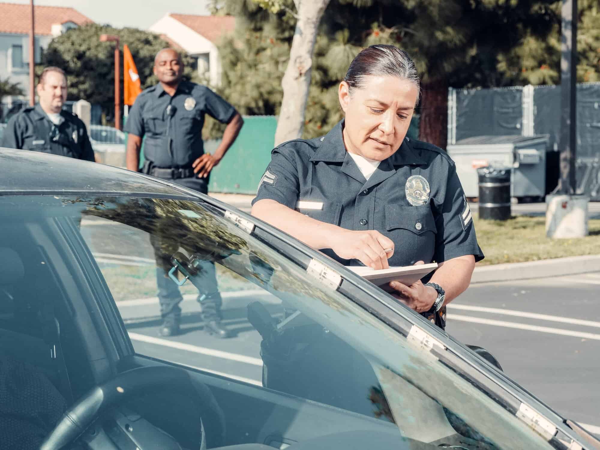 A police officer writes a ticket next to a car as two others look on—much like personal injury lawyers Louisiana review case details.