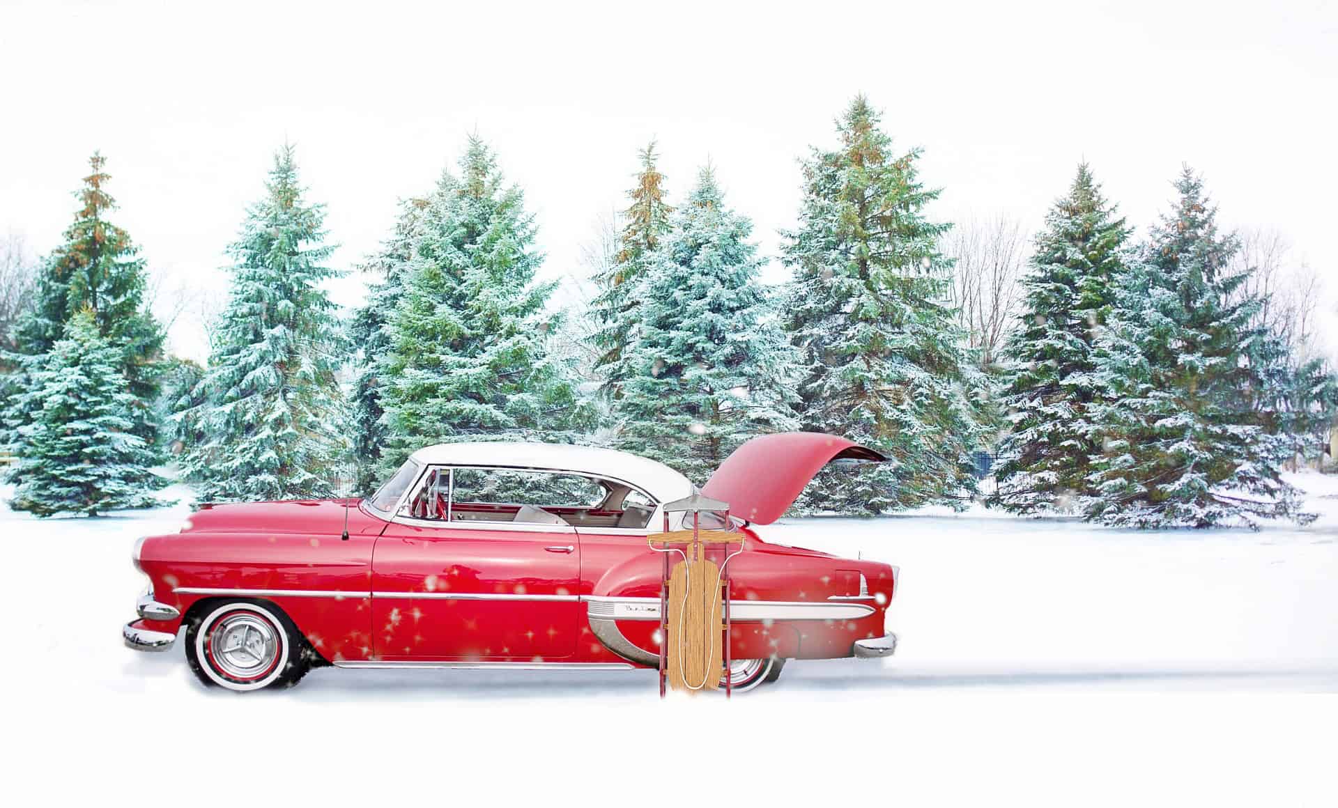 A red vintage car with its trunk open sits in snowy pines; a wooden sled leans against it—perfect for an immigration visa lawyers’ holiday card.