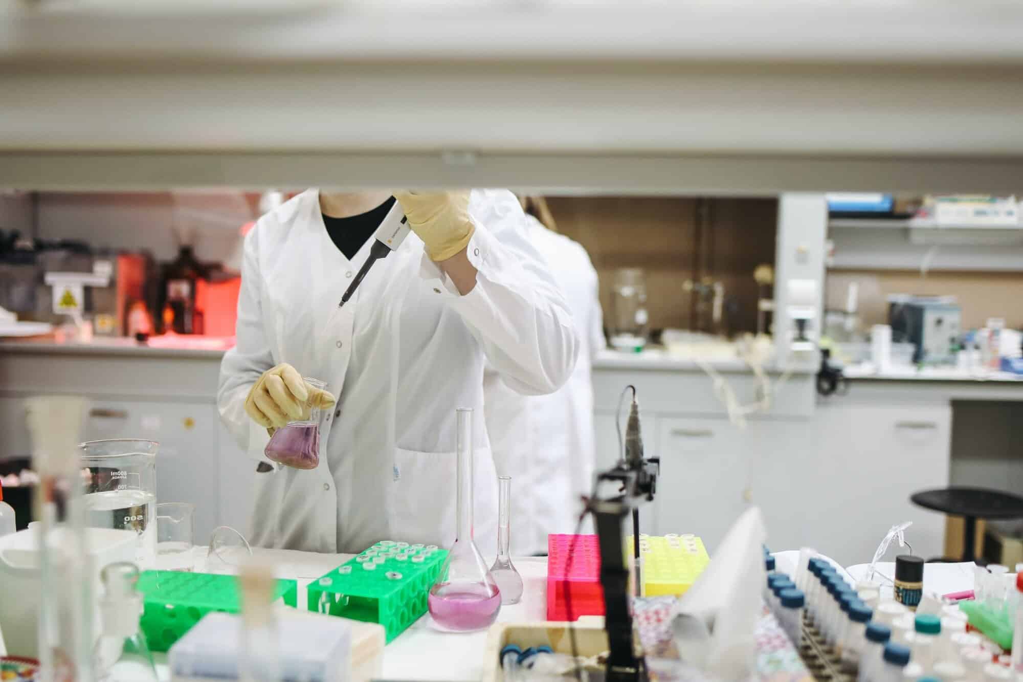 Person in a white lab coat pours purple liquid into a beaker, like immigration visa lawyers handling complex cases with precision.