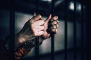 Close-up of hands gripping jail bars, wrists in handcuffs—a stark image often faced by clients of deportation law firms.