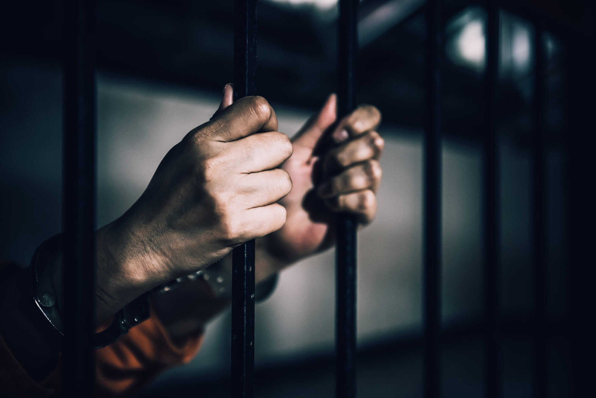 Close-up of hands gripping jail bars, wrists in handcuffs—a stark image often faced by clients of deportation law firms.