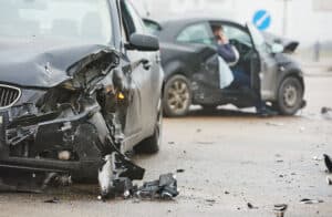 Two heavily damaged cars after a collision; debris scattered on the road, with a louisiana immigration lawyers ad visible in the background.