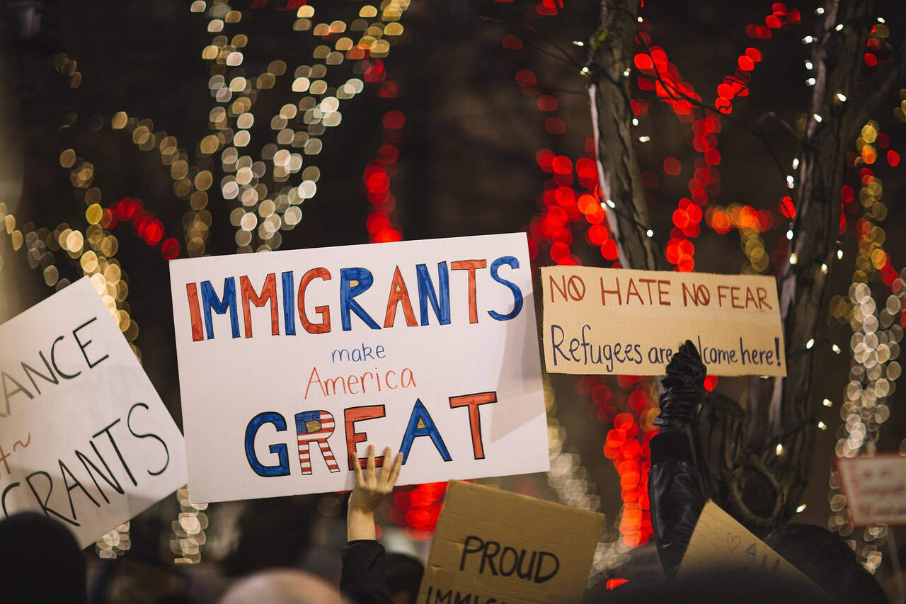 People hold signs at a protest, including "Immigrants make America great," while louisiana immigration lawyers advocate nearby.