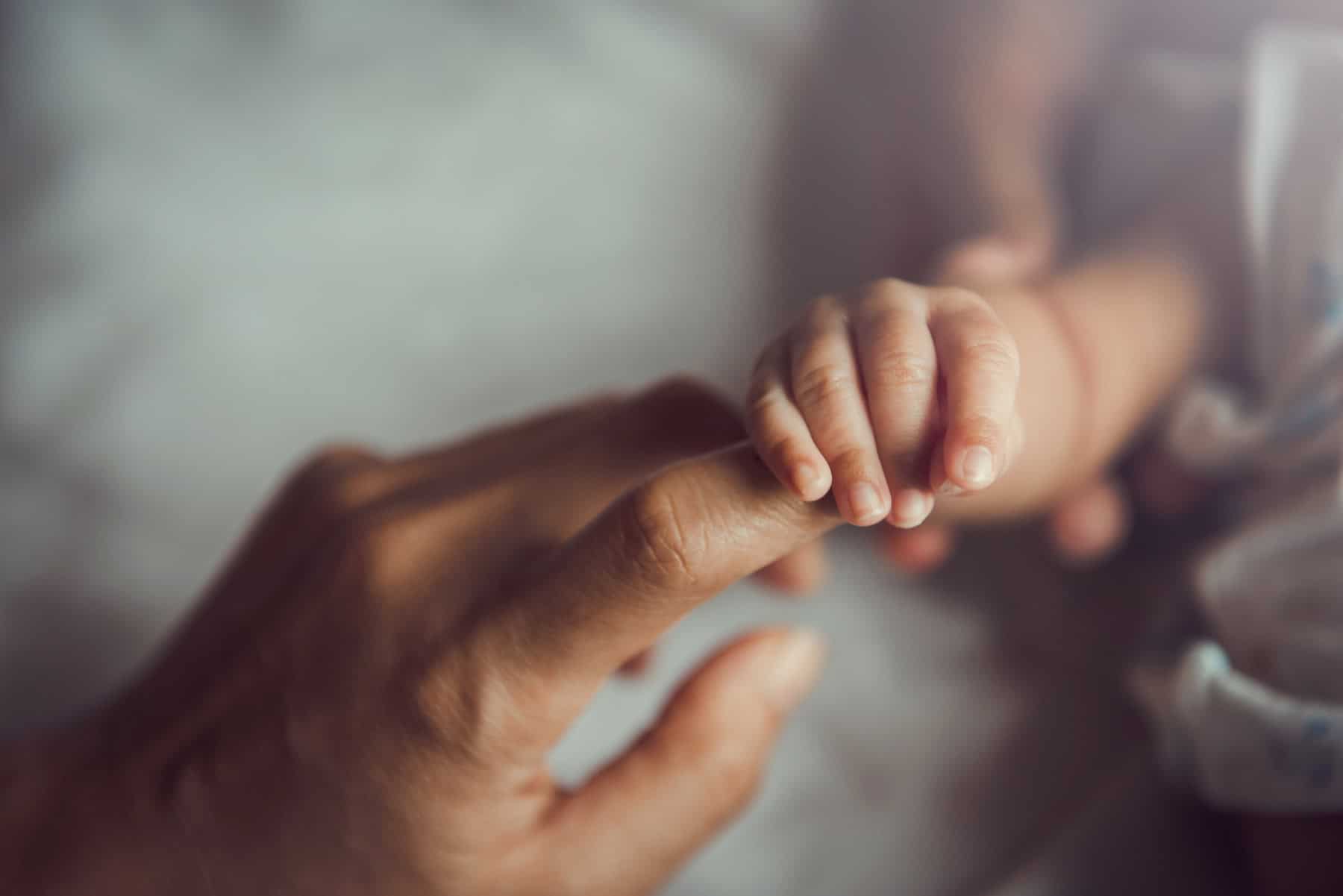 Primer plano de un padre sosteniendo la mano de su bebé recién nacido.