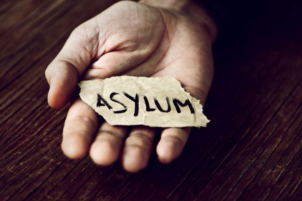 Closeup of a young man's hand holding a piece of paper with the word asylum